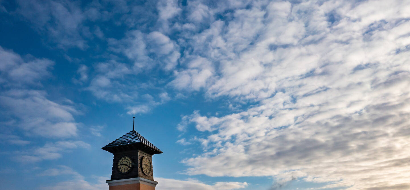 A clock tower stands against a vibrant blue sky dotted with wispy white clouds.